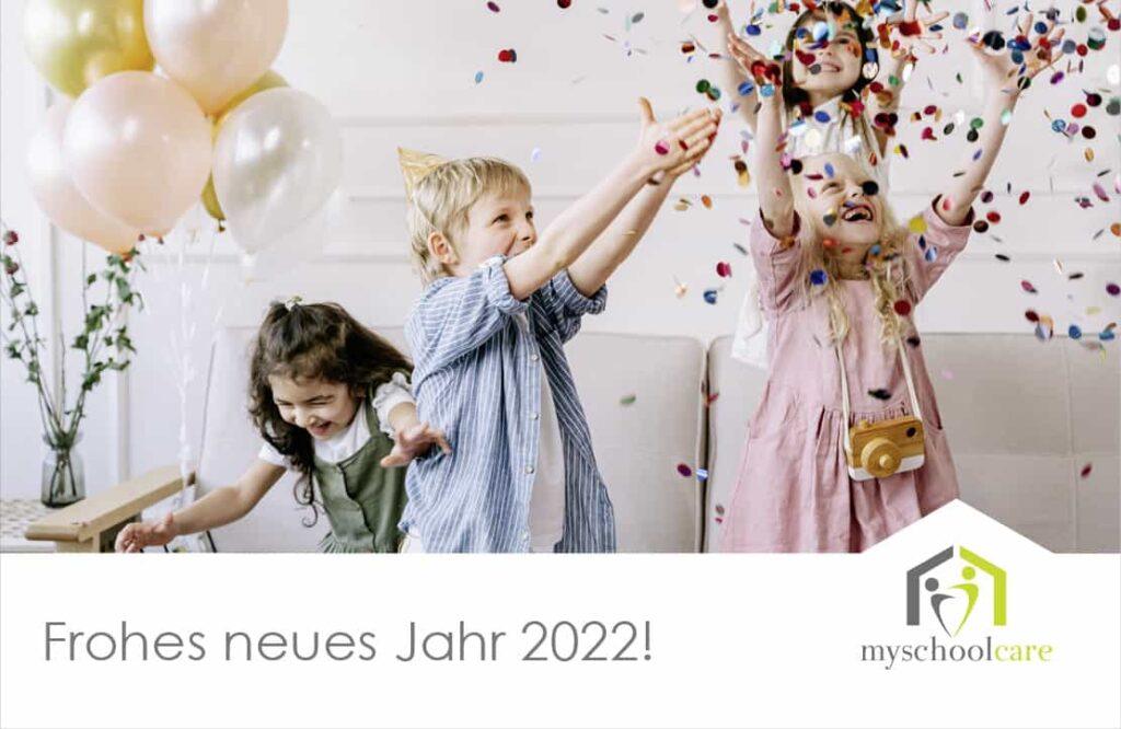 Drei kleine Kinder feiern in einem Haus mit Konfetti. Zwei Mädchen und ein Junge lächeln und spielen in der Nähe von goldenen und rosa Luftballons. Der Text lautet Frohes neues Jahr 2022! mit dem myschoolcare-Logo unten rechts.