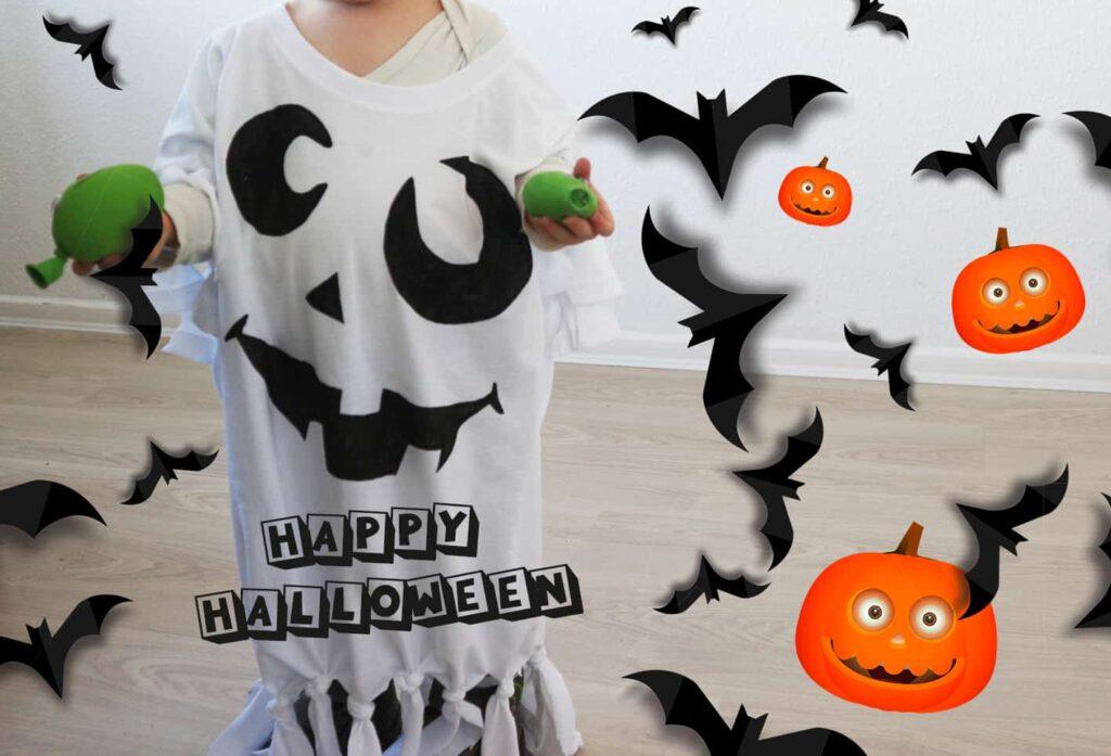 Ein Kind, das ein weißes Geisterkostüm mit einem Gesichtsmuster trägt, hält zwei grüne Objekte. Das Bild zeigt Cartoon-Fledermäuse, lächelnde Irrlichter und die Worte Happy Halloween in Blockbuchstaben.